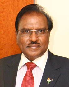 A grayscale image of Dr. Pillrai Pragatiwaym, Pro Chancellor of Vennikulam University, standing confidently with a backdrop of the university campus.